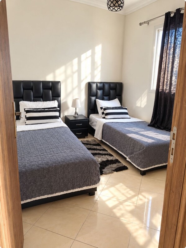 A bedroom with two beds, a nightstand, a lamp, and a window with curtains.