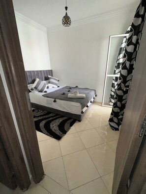 Ein Schlafzimmer mit einem Bett, einem Nachttisch, einer Pendelleuchte, einem gemusterten Vorhang und einer Holztür.