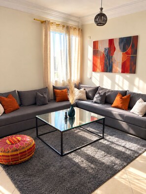 A modern living room with a grey sofa set, a glass coffee table, and a vibrant rug.