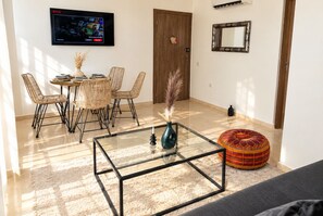 A living room with a glass coffee table, wicker chairs, a television, and a door.