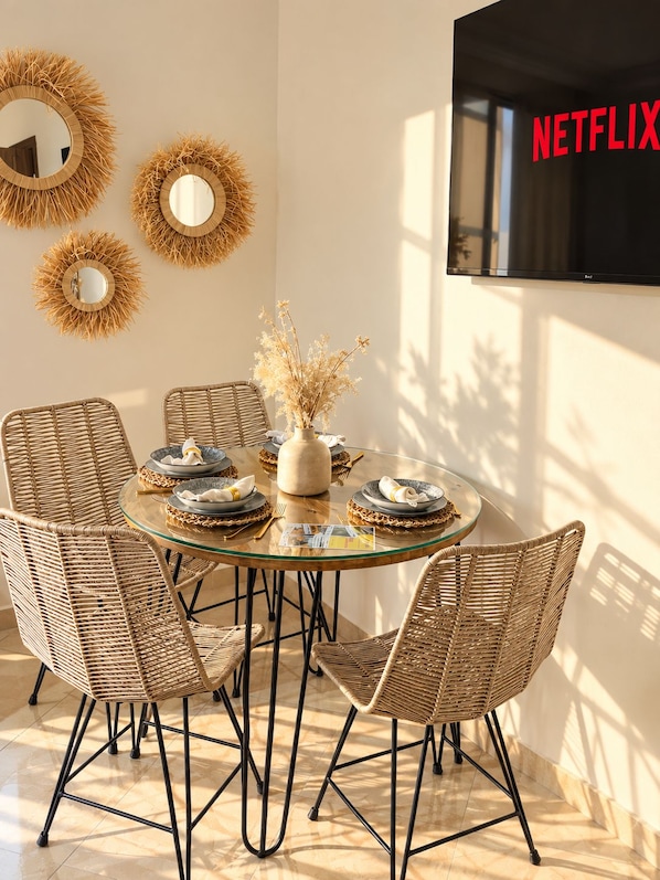 A dining area with a round glass table, wicker chairs, and decorative mirrors on the wall.