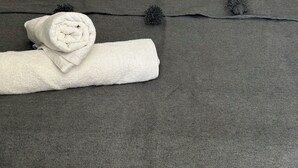 A neatly made bed with grey bedding, two striped pillows, and a rolled white towel on a dark grey headboard.