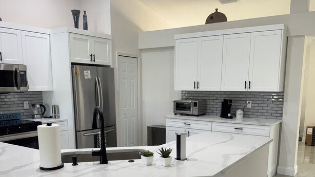 A modern kitchen with white cabinetry, stainless steel appliances, and a marble countertop.