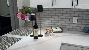 A kitchen with white cabinets, a marble countertop, a wine bottle, a vase with flowers, and a decorative lamp.