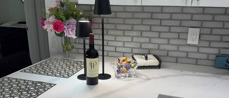 A kitchen with white cabinets, a marble countertop, a wine bottle, a vase with flowers, and a decorative lamp.