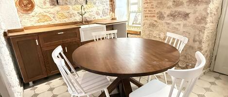 A dining area with a round wooden table surrounded by white chairs, a stone wall, and a rustic ceiling.
