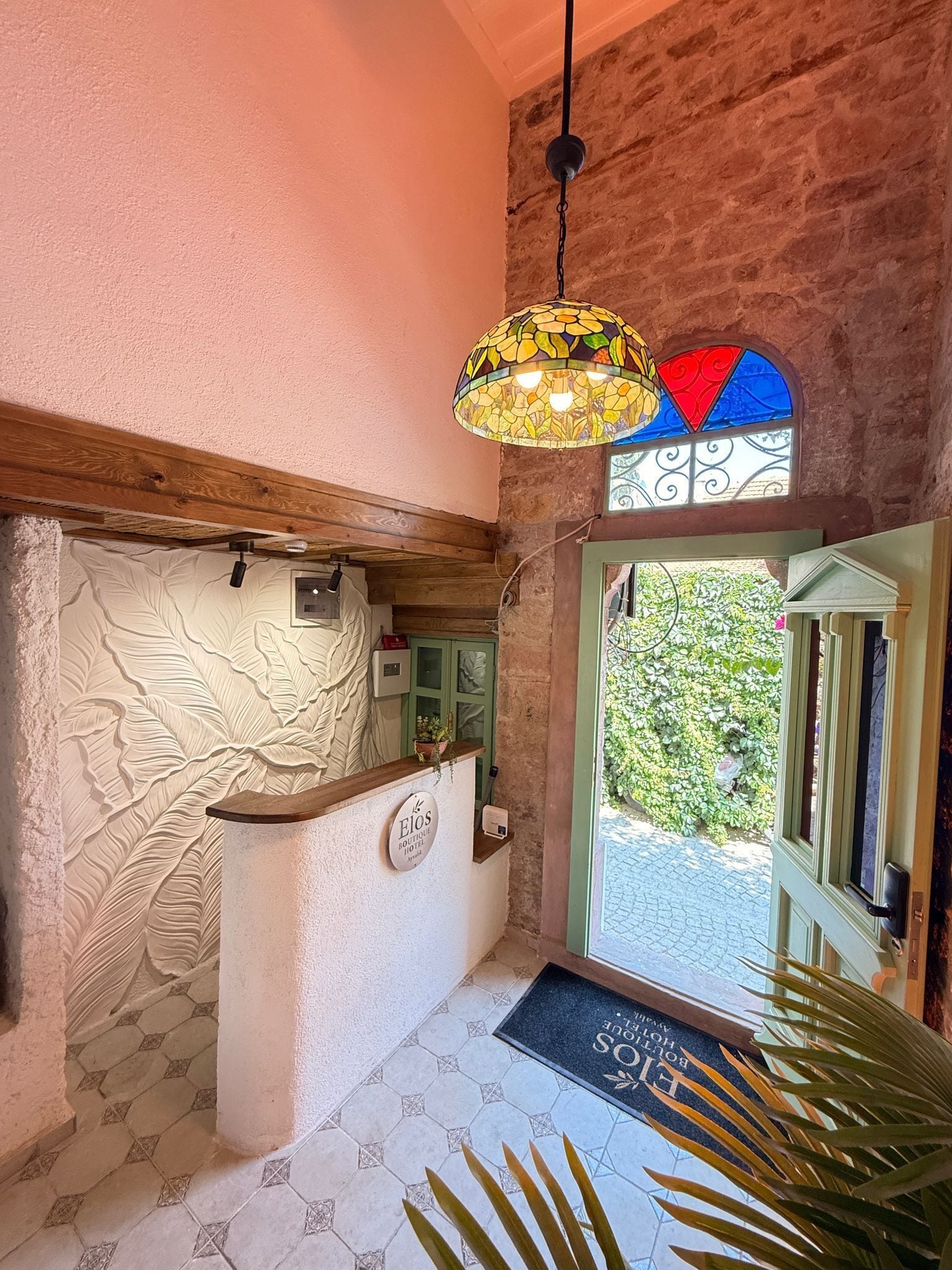 A reception area with a wooden reception desk, a mosaic ceiling light, a stained glass window, and a door leading outside.