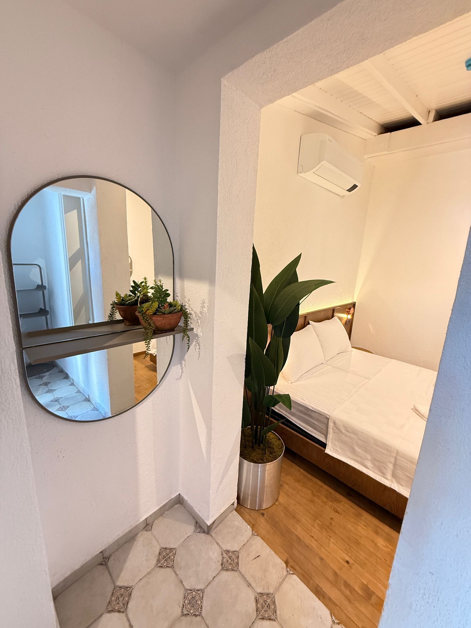A bedroom with a bed, a round mirror, a potted plant, and a small table.
