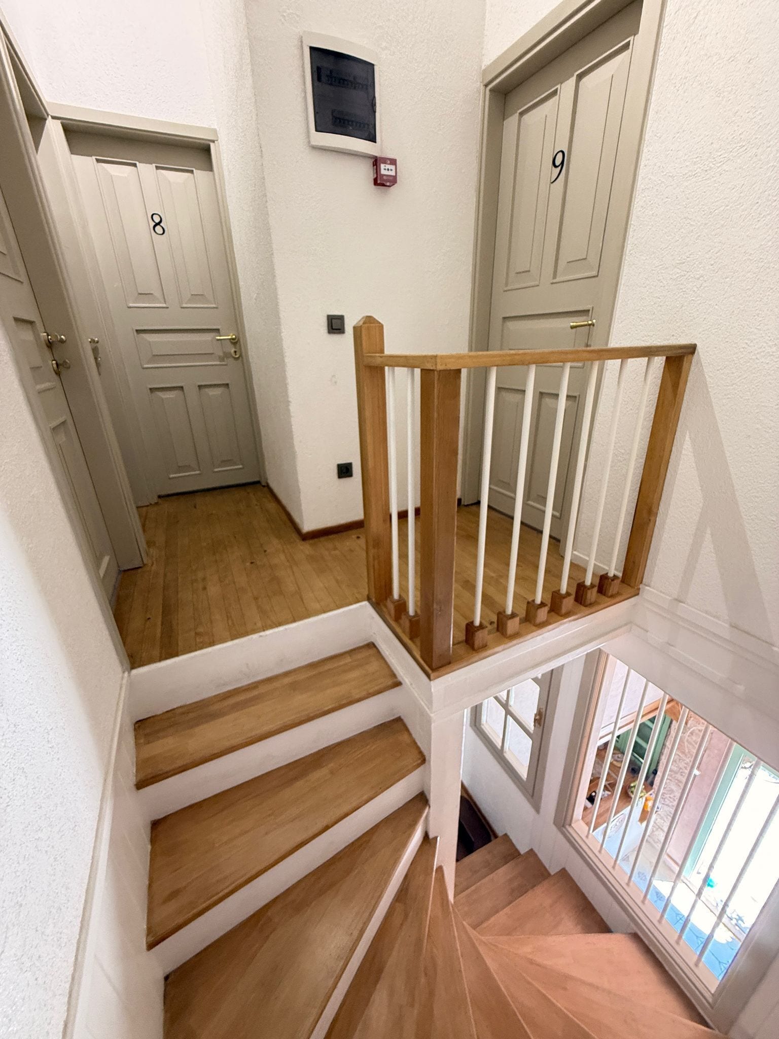 A staircase with wooden steps and a wooden handrail, leading to a landing with two doors, one marked with the number 8 and the other with the number 9.