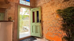 Un pasillo con una puerta verde, un vitral y una lámpara colgante.