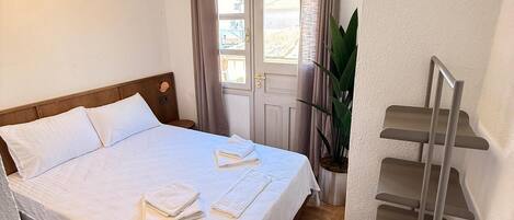 A hotel room with a bed, a bedside table, a plant, and a built-in shelf unit.