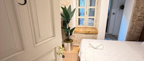 A bedroom with a stone wall, a bed with white linens, a potted plant, and a door marked with the number 3.