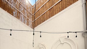 Una habitación con pared blanca, cerca de una valla de madera, un sofá beige con cojines e iluminación con luces colgantes.