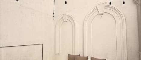 A room with a white wall, a wooden fence, a beige sofa with cushions, and string lights.