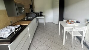 Cozinha compacta com fogão, micro-ondas e pia. Há uma pequena mesa de jantar com cadeiras e um armário branco.