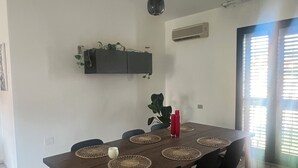 Uma sala de jantar com mesa de madeira, cadeiras pretas, jogos americanos de tecido trançado e luminária pendente.