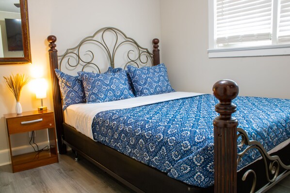 A neatly made bed with a patterned bedspread, a wooden nightstand with a lamp, and a mirror on the wall.