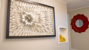 Una stanza con un'ampia opera d'arte astratta appesa al muro, uno specchio circolare rosso e un piccolo ripiano bianco con un ornamento dorato.