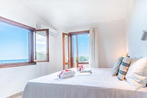A hotel room with a bed, a window with curtains, and a view of the sea. - House Sardinia La Dolce Vita (Budoni)