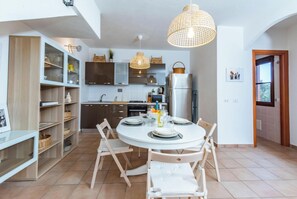 A modern kitchen with a dining area, wooden cabinets, a white dining table, and a hanging light fixture.