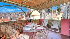 A rooftop terrace with a table set for dining, chairs, a decorative plant, and a view of the cityscape. - La Casa Della Vikinga With Sea-view Terrace (Sanremo)