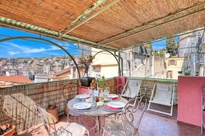 Terraza en la azotea con una mesa dispuesta para comer, sillas, una planta decorativa y vistas de la ciudad.