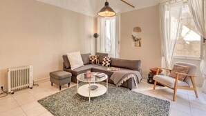 A living room with a sofa, ottoman, coffee table, and a chair. There is a radiator, a lamp, and a window with curtains. - La Casa Della Vikinga With Sea-view Terrace (Sanremo)