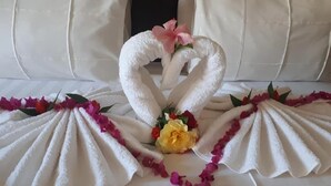 Una cama con una toalla dispuesta en forma de cisne, decorada con flores y pétalos rosados.