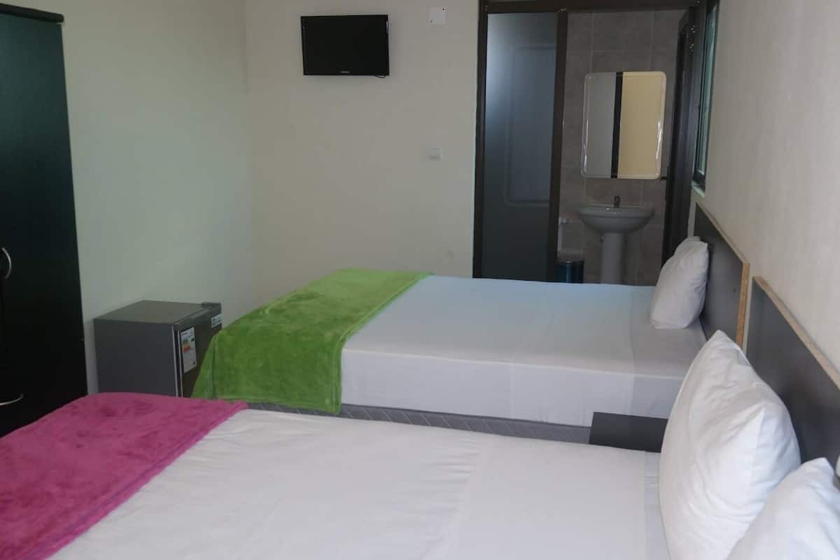 A hotel room with two beds, a small desk, a mirror, and a sink.