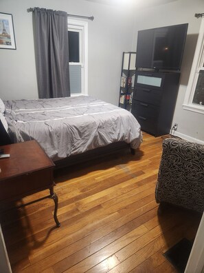 Cozy retreat with a single bed, desk, and TV, plus a bookshelf and comfortable seating area.