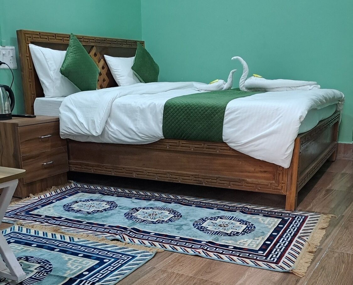 A bedroom with a wooden bed, green pillows, a white blanket, and a patterned rug.