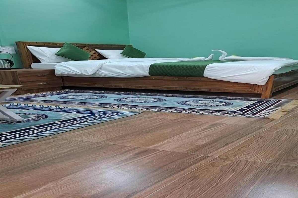 A bedroom with a wooden bed, green pillows, a patterned rug, and a nightstand.