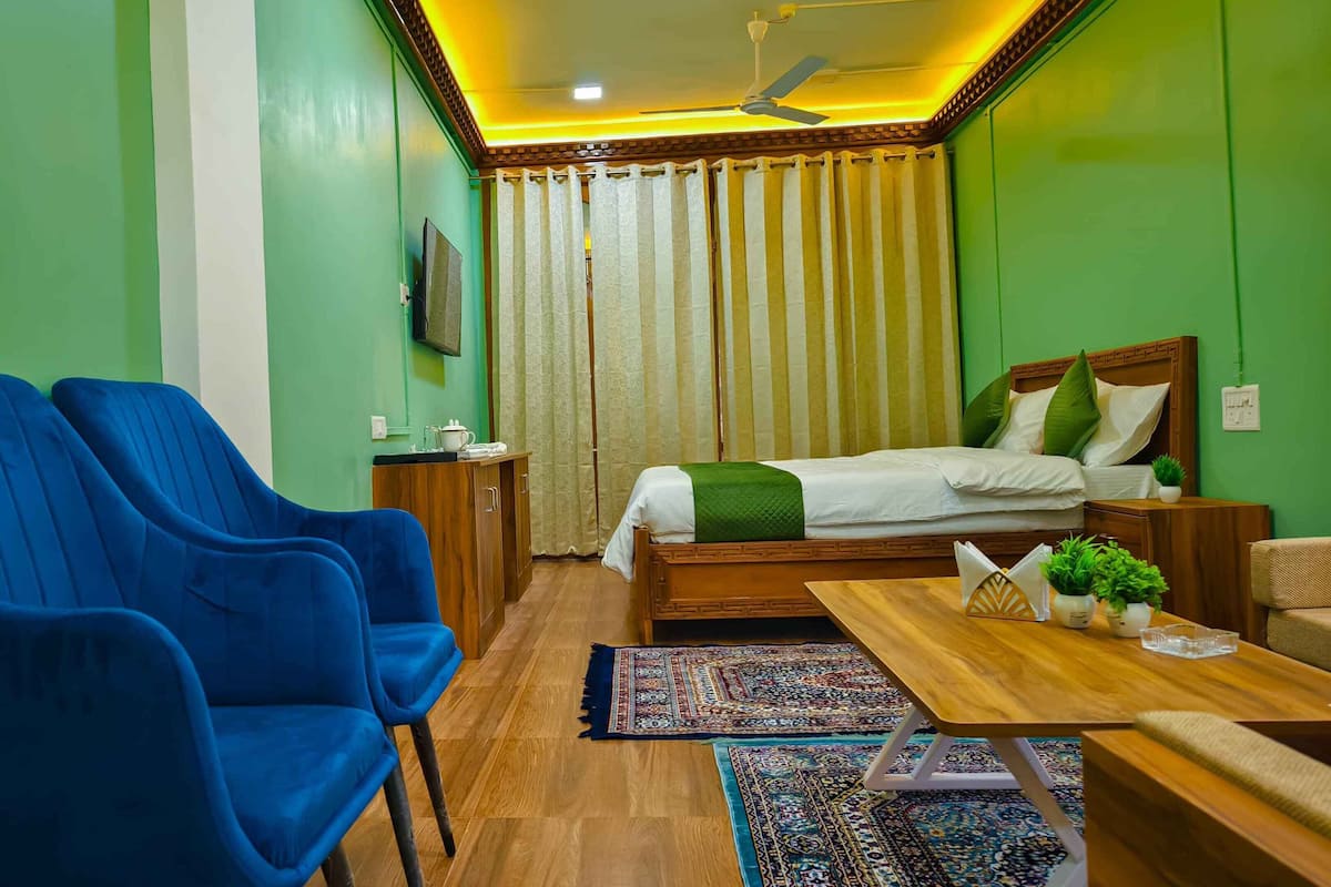 A room with a bed, two blue chairs, a wooden table, a TV, and a patterned rug.