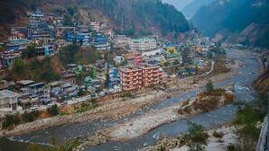 A riverside town with buildings along the riverbank, surrounded by hills. - Mudita Hotel (West Kameng)