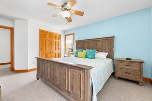 A bedroom with a wooden bed, a nightstand, a ceiling fan, and a door. - 🏖 Ocean Views! 🌅Heated Pool, 🎯Game Room, 💦Hot Tub, Mini Golf & Steps to Sand (Nags Head)