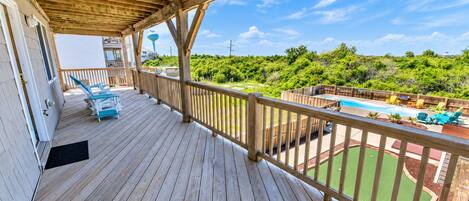 A wooden deck with a pool, lounge chairs, and a view of a lush landscape.