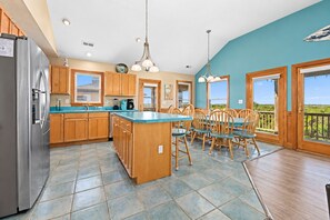 A spacious kitchen with a central island, wooden cabinets, and a large window overlooking a scenic view. - 🌊Redheaded Mermaid: Ocean Views, Heated Pool, Hot Tub, Mini Golf, Steps to Sand (Nags Head)