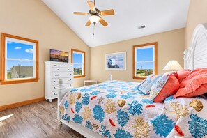 Une chambre à coucher comprenant un lit, une commode, un ventilateur de plafond et deux fenêtres donnant sur un paysage agréable.