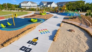Une aire de jeux avec un jeu de marelle, un bac à sable et des balançoires.