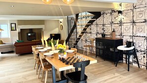 A dining area with a wooden table set for six, a chessboard, and a staircase with a patterned wall. - Koquillage, Cozy House with Spa, GR34, Sleeps 10, Near the Ocean (Moëlan-sur-Mer)