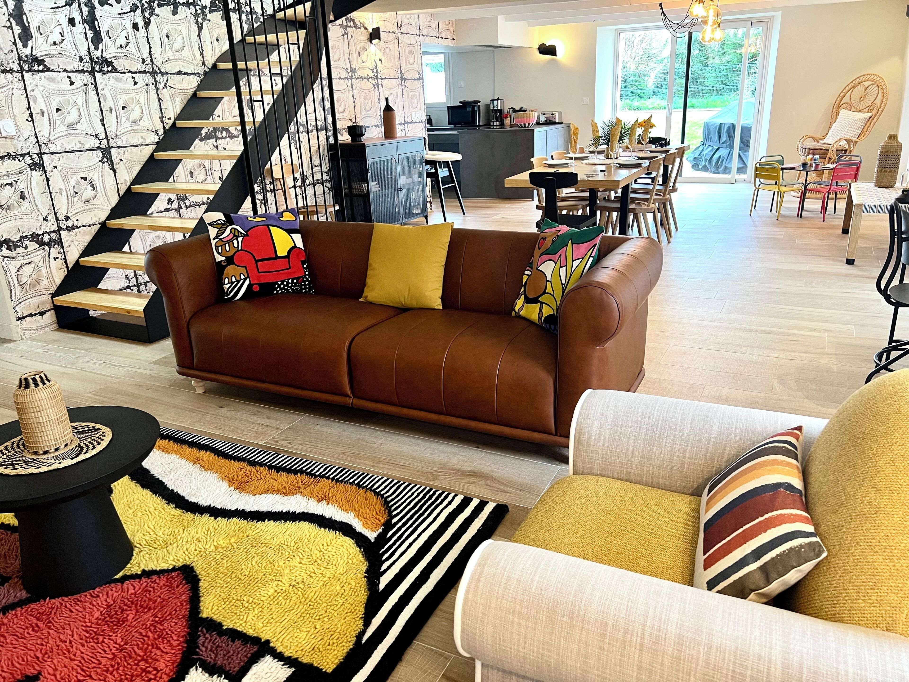 A spacious living area with a brown leather sofa, a patterned rug, and a dining table with chairs.
