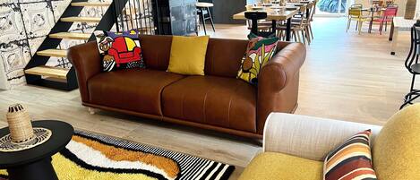 A spacious living area with a brown leather sofa, a patterned rug, and a dining table with chairs.