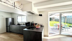 A modern kitchen with a central island, a dining area with outdoor seating, and a view of a garden. - Koquillage, Cozy House with Spa, GR34, Sleeps 10, Near the Ocean (Moëlan-sur-Mer)