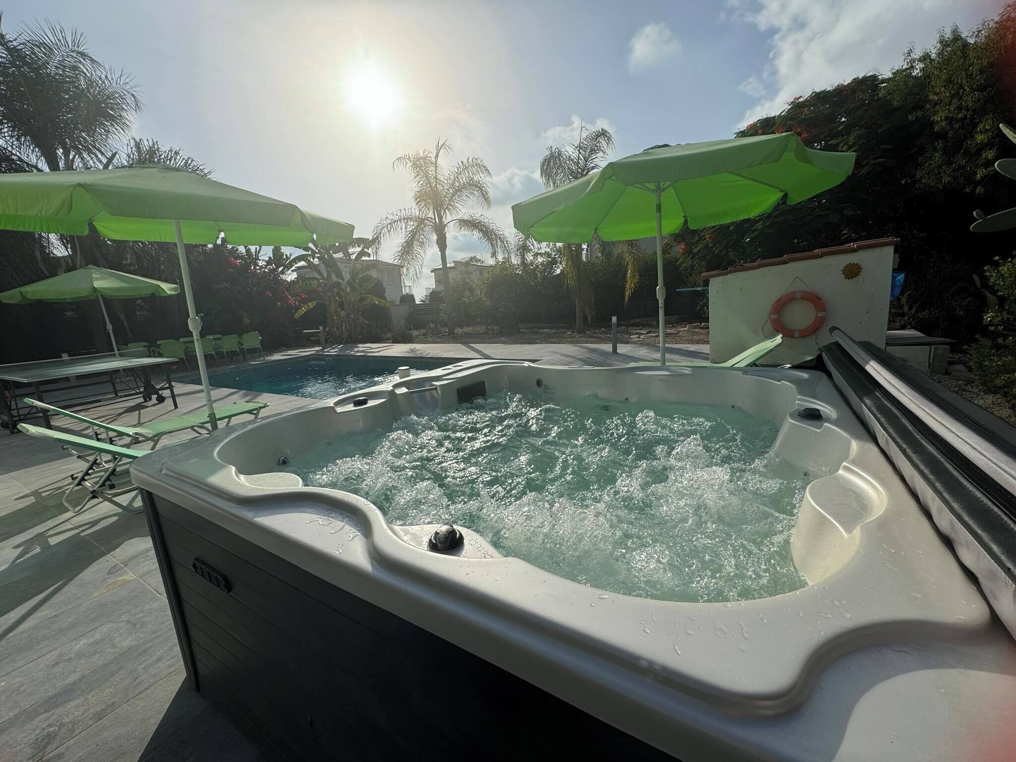 Ein Whirlpool mit Pool, umgeben von grünen Sonnenschirmen und einem Rettungsring auf einem Boot.