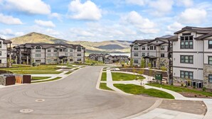 A residential area with modern multi-story buildings, a curved road, and a mountainous backdrop.