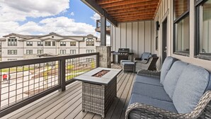 A balcony with a wooden ceiling, wicker furniture, a barbecue grill, and a view of a residential building.
