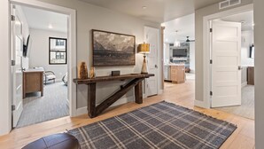 A modern interior with a wooden console table, a large landscape painting, and a kitchen in the background.