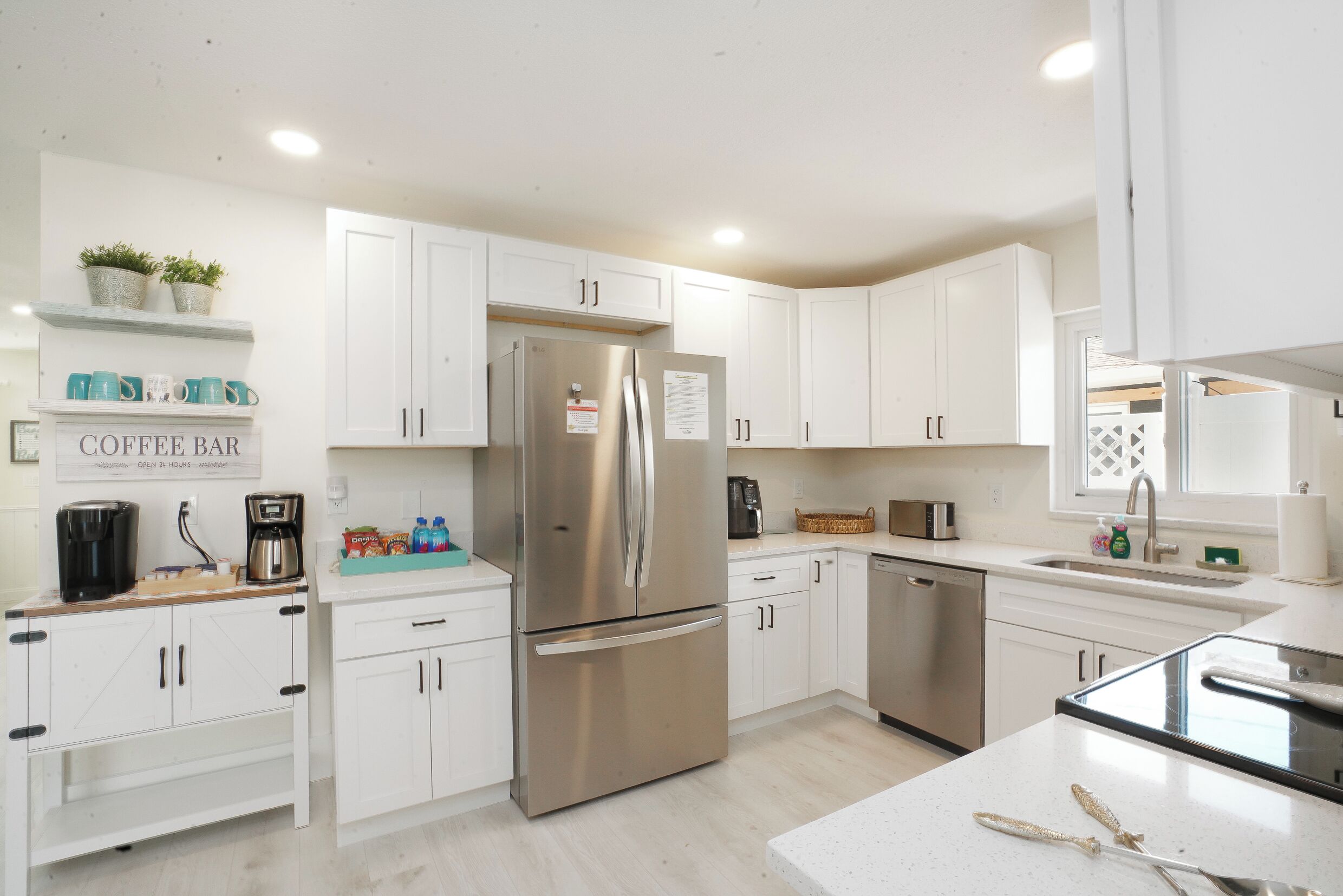 A modern kitchen with white cabinets, a stainless steel refrigerator, a coffee bar sign, and a sink.