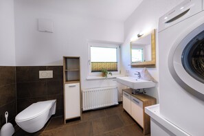 Enjoy a functional and uncluttered bathroom with a sleek toilet, compact sink area, and washing machine.