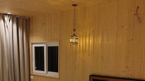 Ein Schlafzimmer mit Holzbalkendecke, einem Bett mit weißer Bettwäsche, einem Fenster und einer Pendelleuchte.